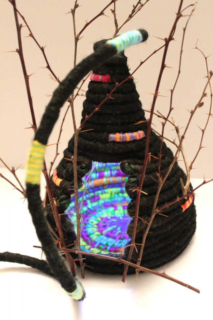 Black wool rope basket illuminated from within, showing bright colours woven inside. The exterior is protected with thorns