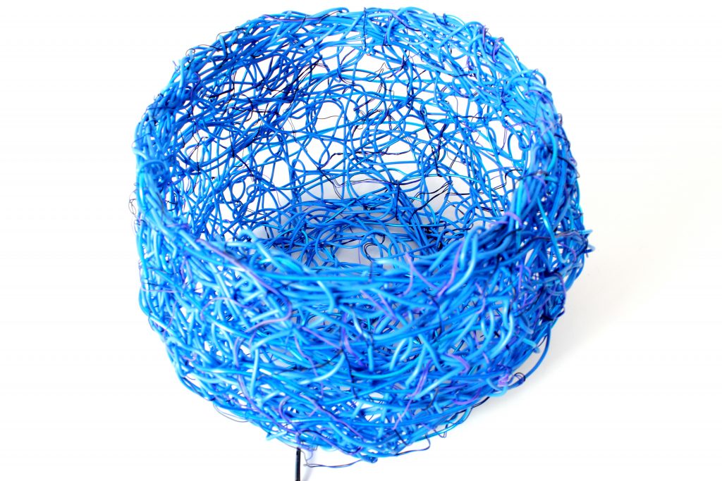 Neon blue electric luminescent wires woven to form a loose tangled-weave basket.